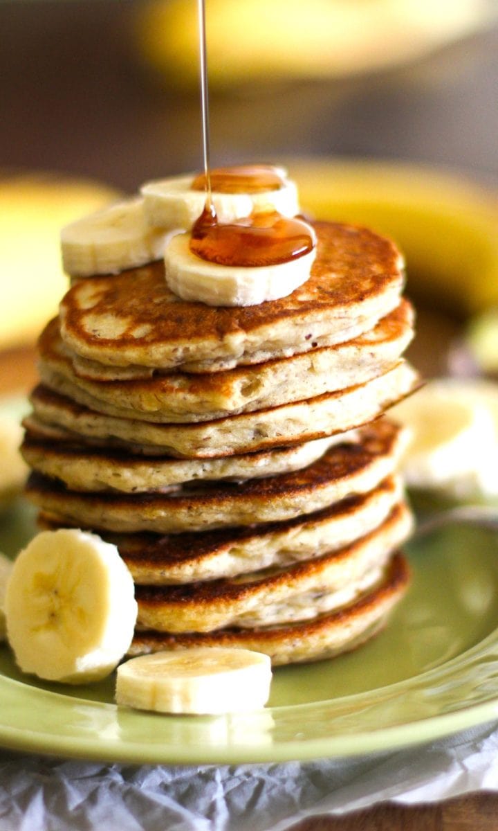 Gluten-Free Vegan Banana Pancakes on a green plate with sliced bananas on top with pure maple syrup being drizzled on top. Ready to eat.