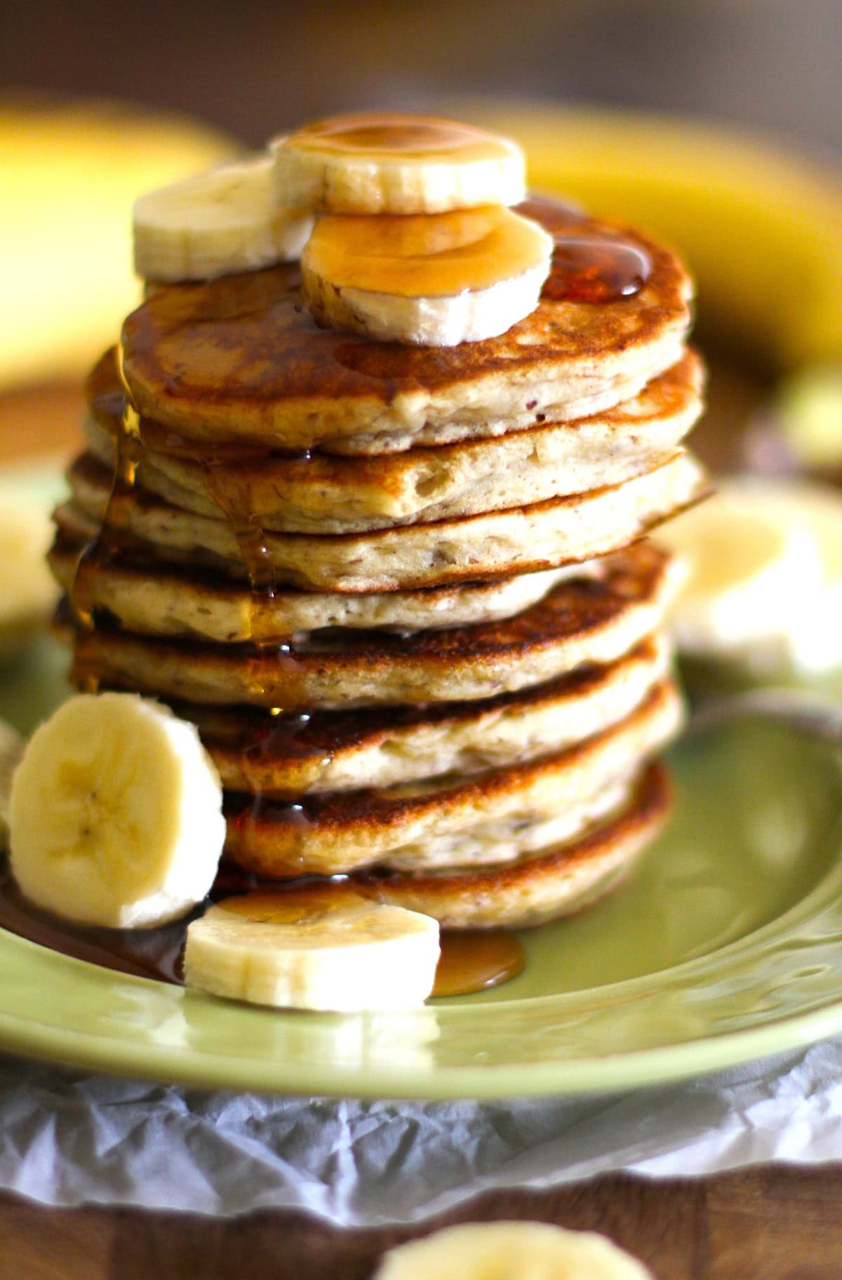 Vegan Banana Pancakes on a plate with sliced bananas on top and pure maple syrup running down the pancakes. Ready to serve!