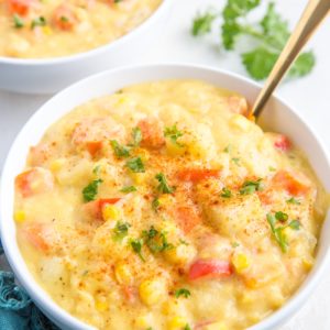 Two big white bowls full of vegan corn chowder, sprinkled with fresh chopped parsley and a dark blue napkin to the side.