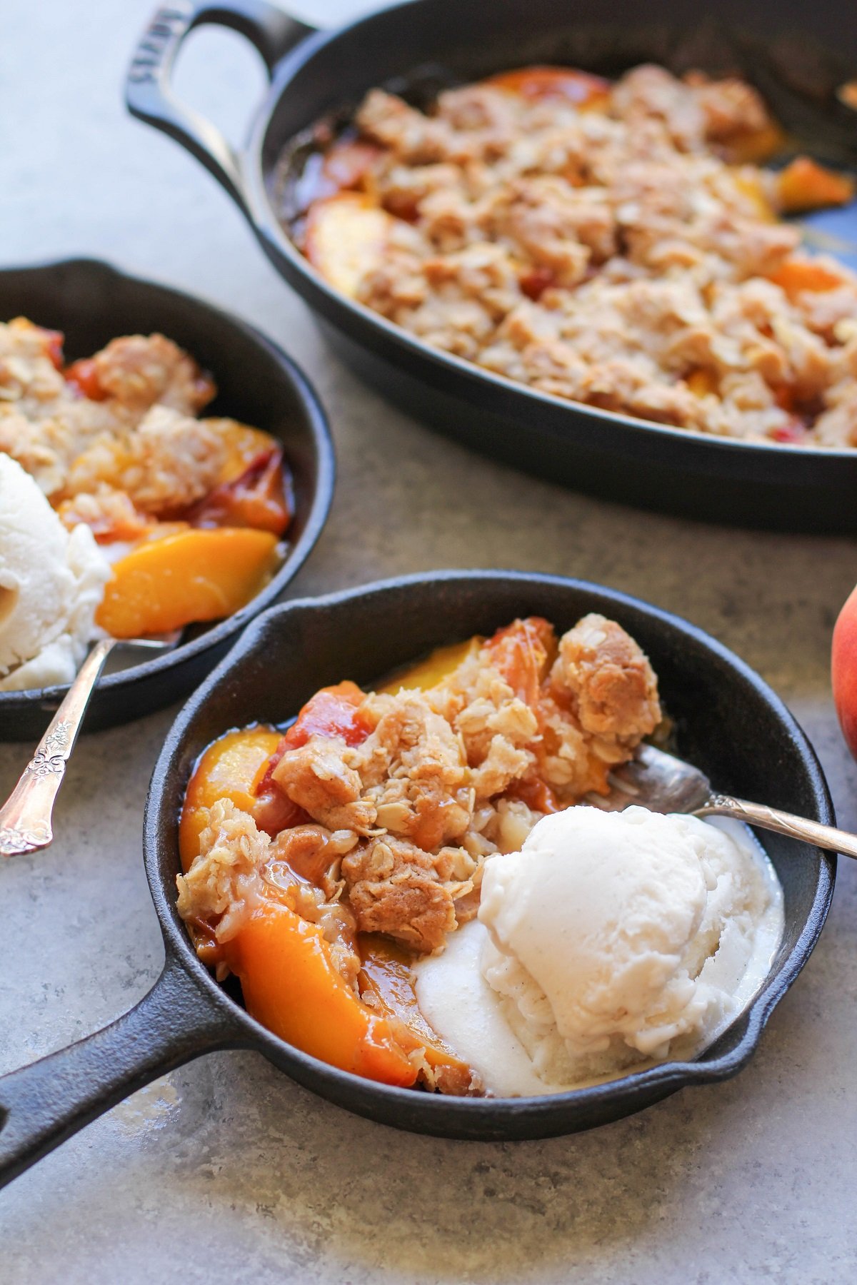 Gluten-Free Vegan Peach Crisp in two small cast iron skillets for individual portions with vanilla ice cream.
