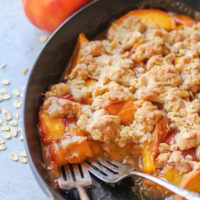 Gluten-Free Vegan Peach Cobbler in a cast iron casserole dish with two forks, ready to eat.