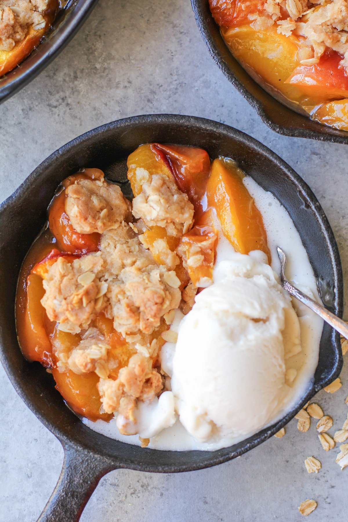 Close up of a single serve of peach cobbler in a small skillet with a melted scoop of vanilla ice cream.