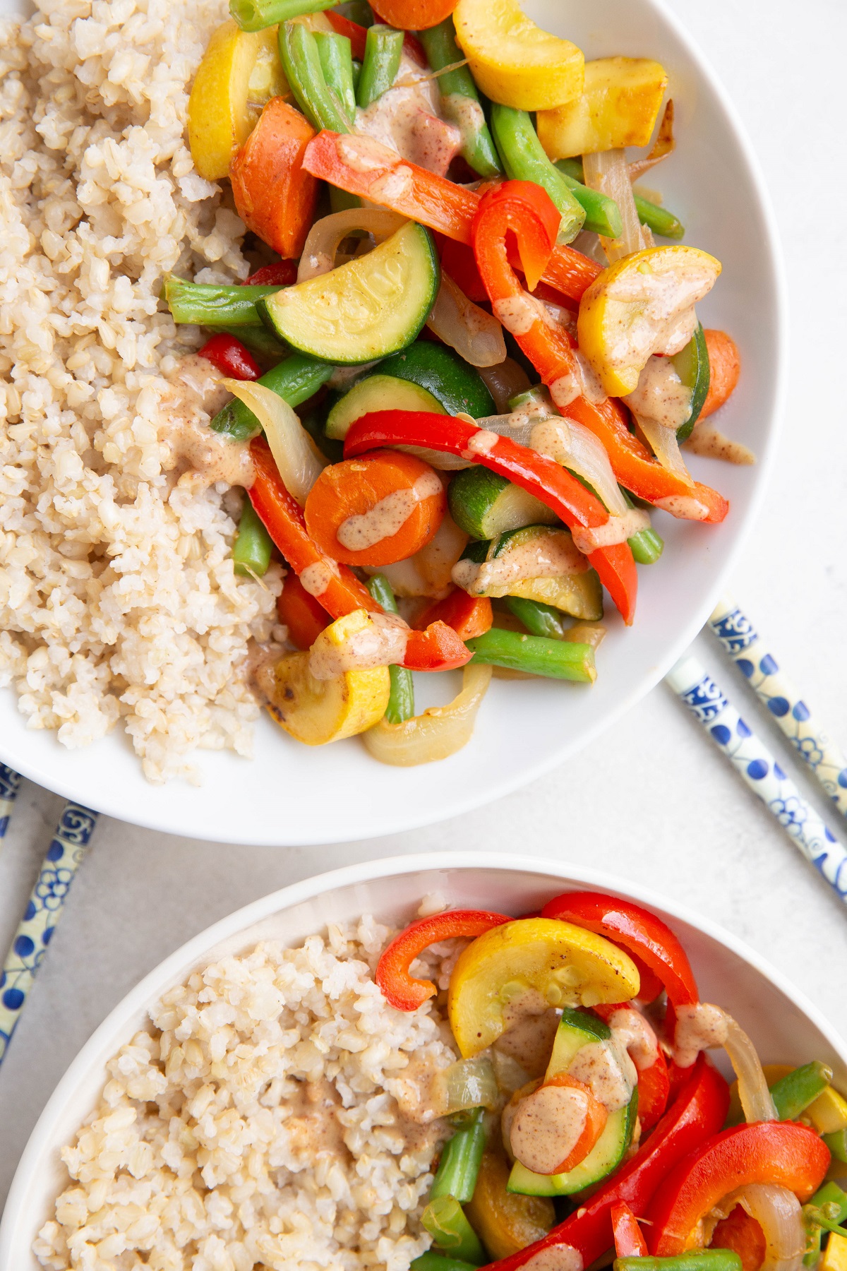 Two white bowls of brown rice and vegetable stir fry.