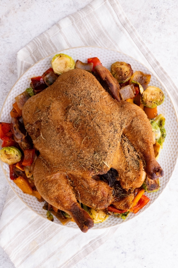 Whole smoked chicken on a plate on top of roasted vegetables, fresh off the smoker grill and ready to serve.