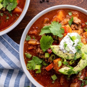 Two bowls of turkey chili with avocado and sour cream on top. A napkin and fresh parsley to the side.