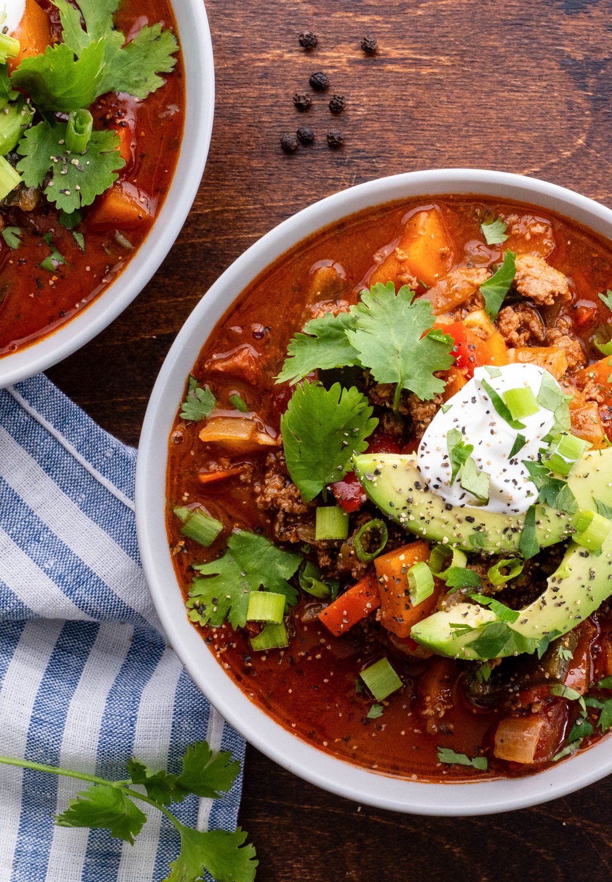 Two bowls of turkey chili with avocado and sour cream on top. A napkin and fresh parsley to the side.