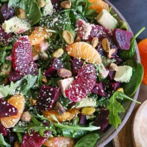 Bowl of citrus roasted beet salad with greens, avocado, hemp seeds and pistachios.