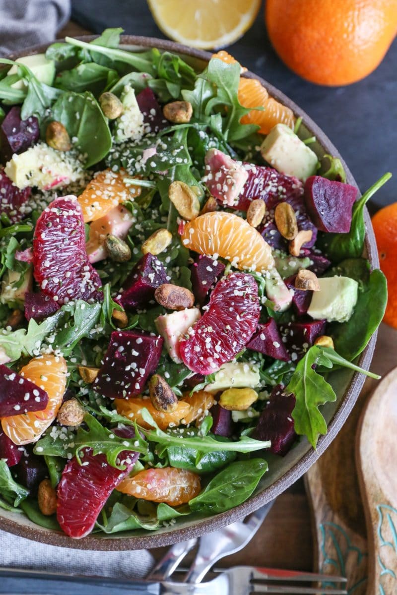 Bowl of citrus roasted beet salad with greens, avocado, hemp seeds and pistachios.