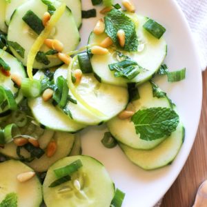 Zesty Cucumber Salad with Pine Nuts on a white plate with green onions and mint leaves and a fork to the side.