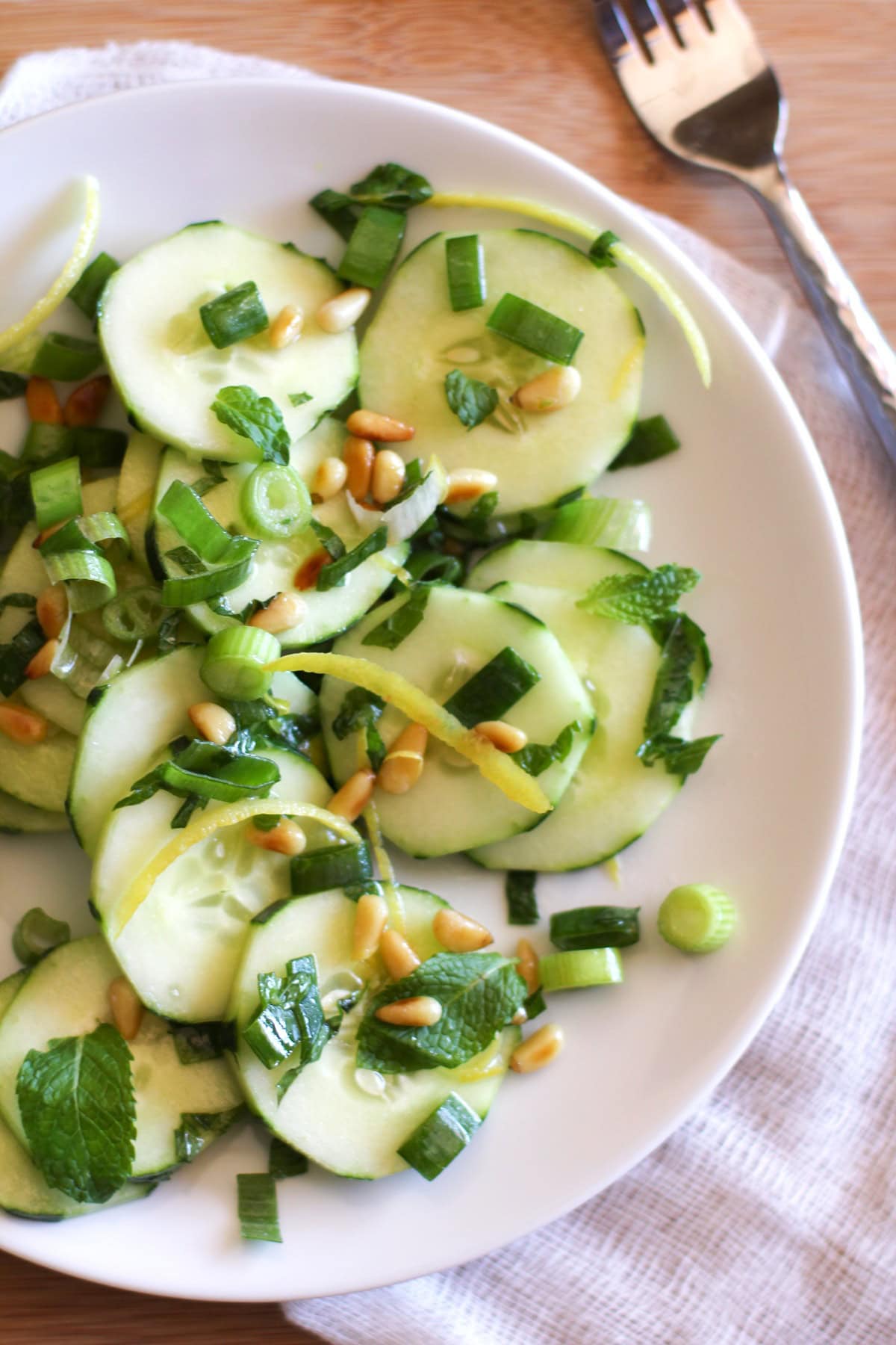 Cucumber salad on a plate with fresh herbs and pine nuts.