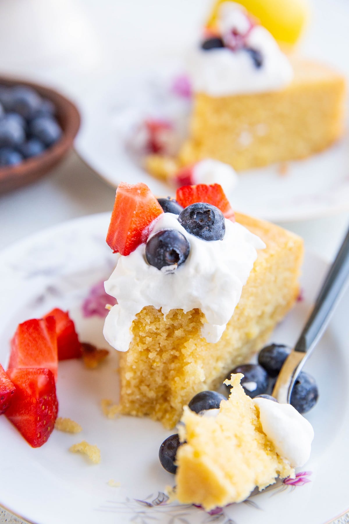 Slice of Almond flour lemon cake with whipped cream and berries on top with a bite taken out.