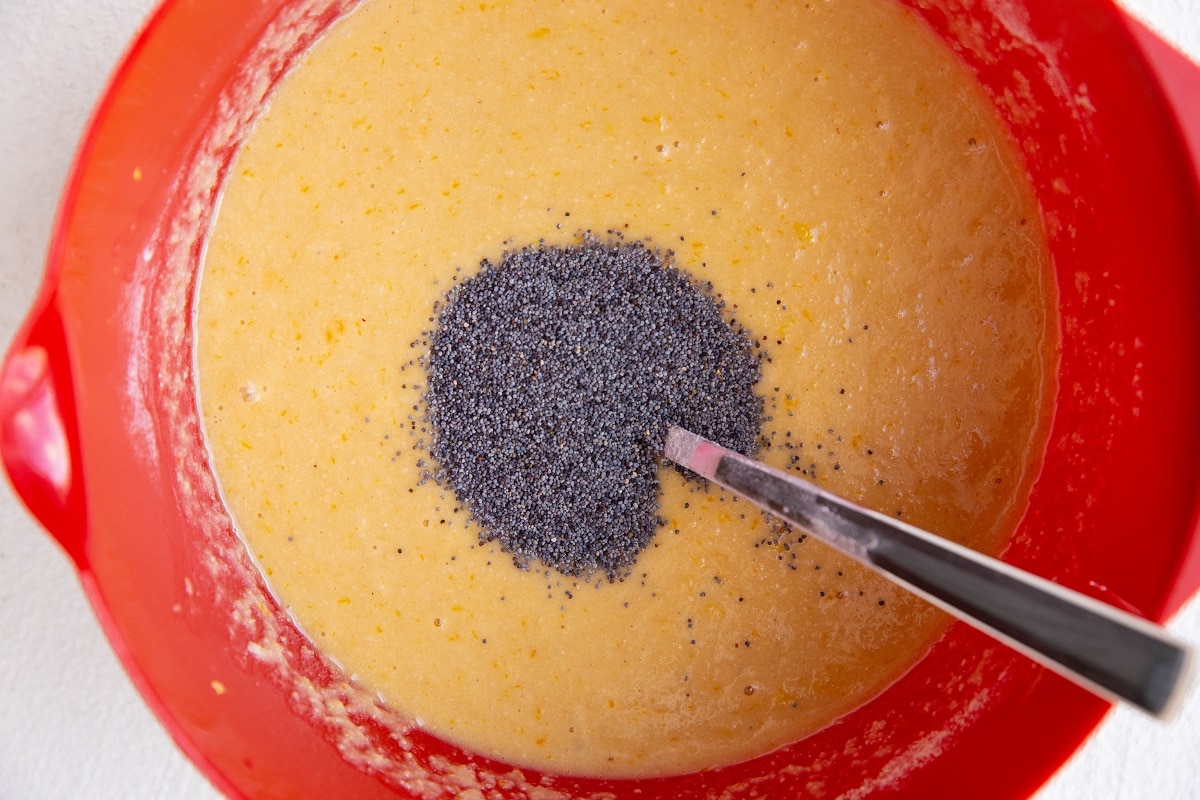 Lemon poppy seed bread batter in a mixing bowl with poppy seeds on top ready to be mixed in.