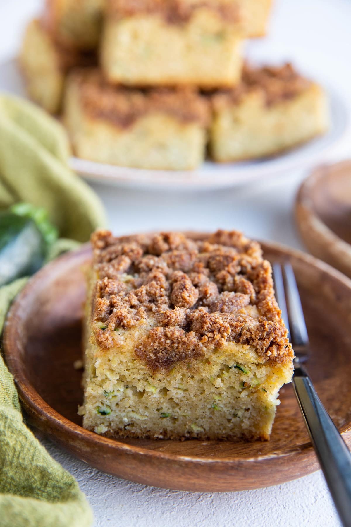 Wooden plates with slices of zucchini crumb cake and a plate of slices in the background.