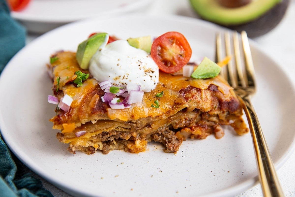 White plate with a hunk of enchilada casserole on top and a golden fork. Ready to eat.