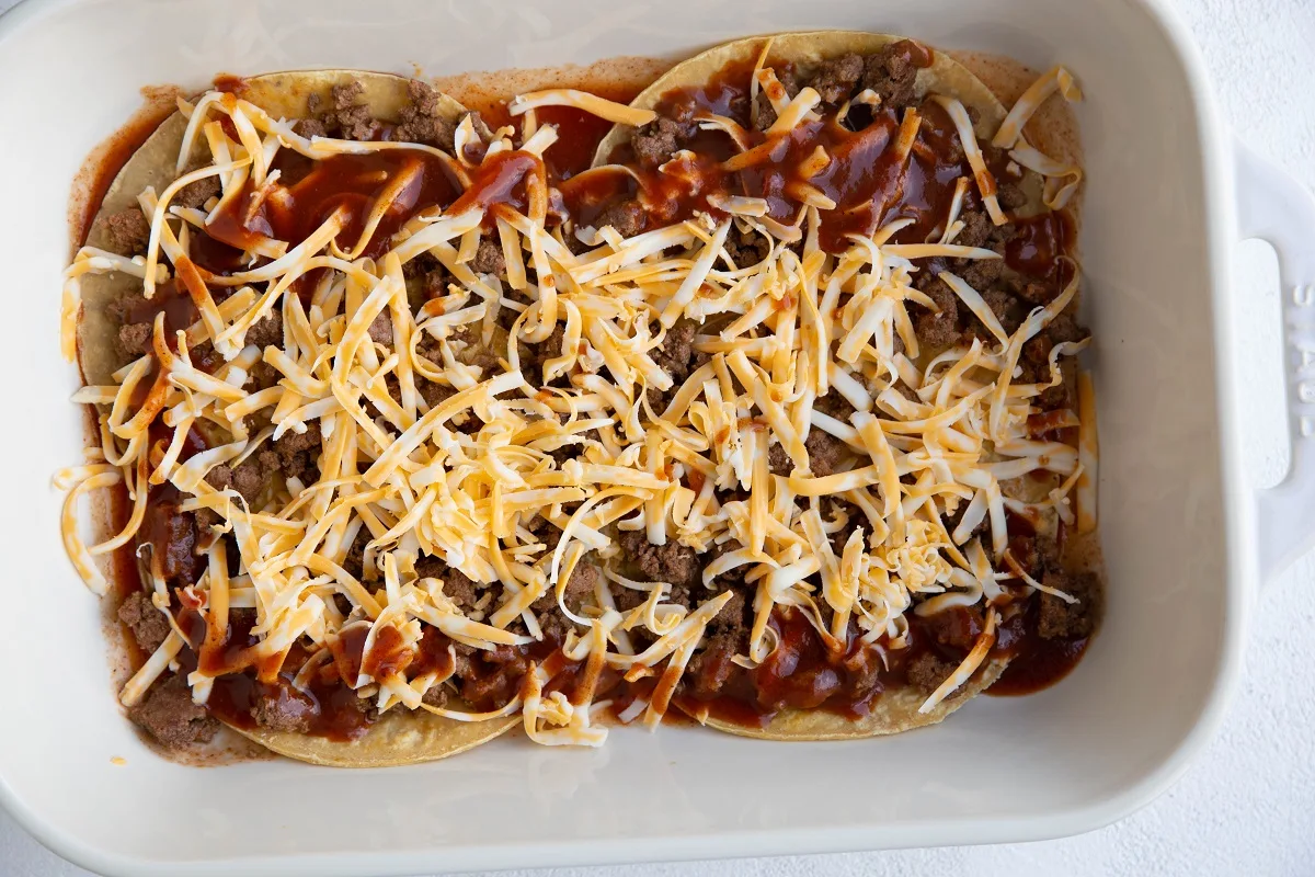 Layer of ground beef, enchilada sauce and shredded cheese on top of corn tortillas.
