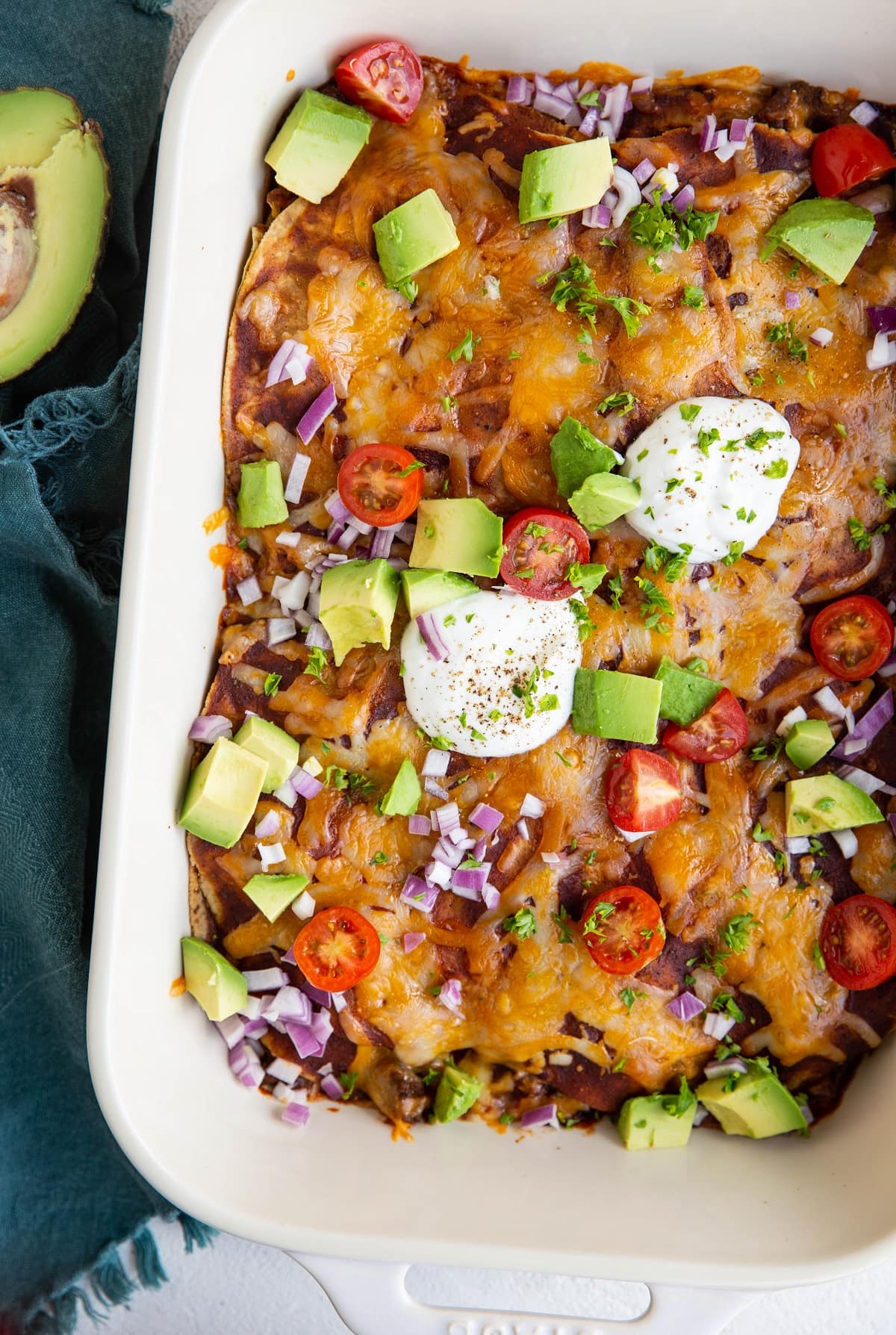Casserole dish of enchilada casserole with avocado, sour cream, tomatoes and onions on top.