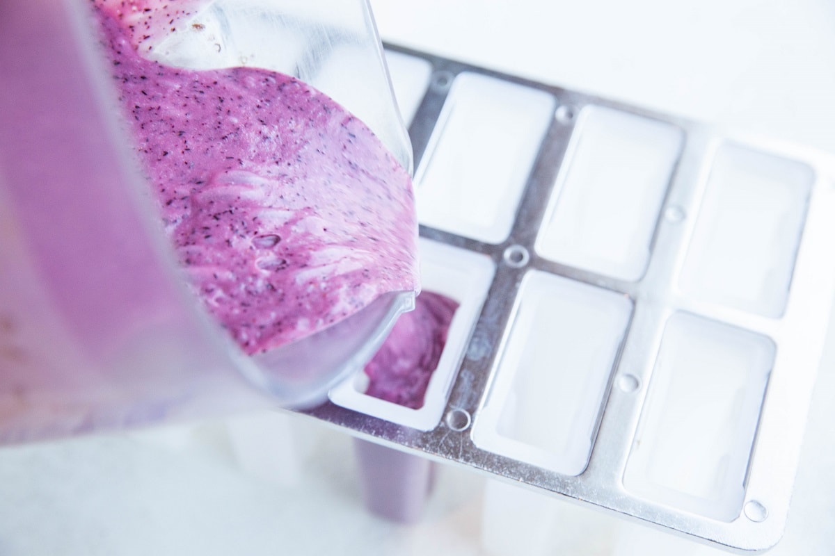 Pouring blueberry mixture from a blender to a popsicle mold to make popsicles.