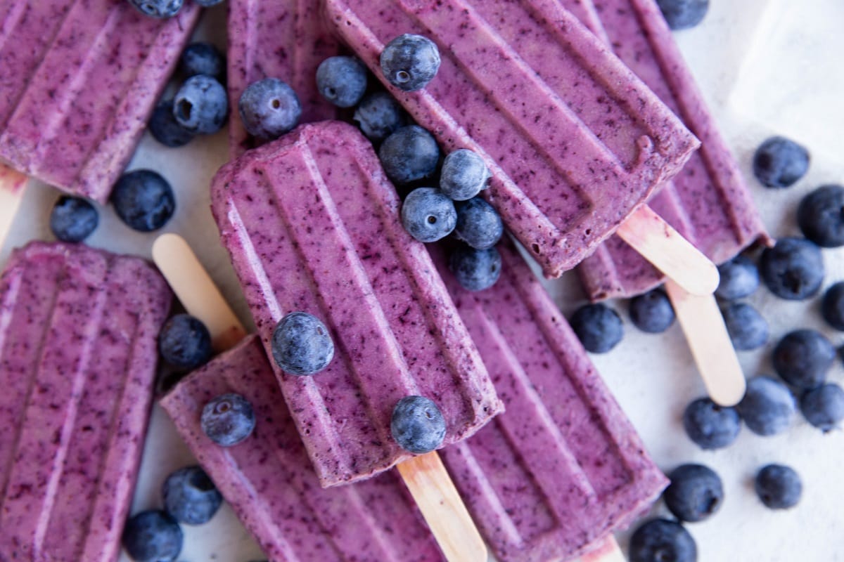 Pile of blueberry coconut milk popsicles with fresh blueberries all around.