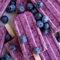 Stack of blueberry coconut milk popsicles with fresh blueberries all around.