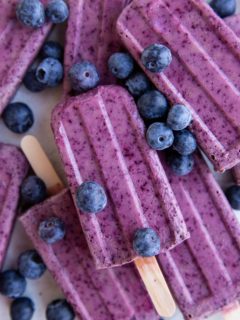 Stack of blueberry coconut milk popsicles with fresh blueberries all around.