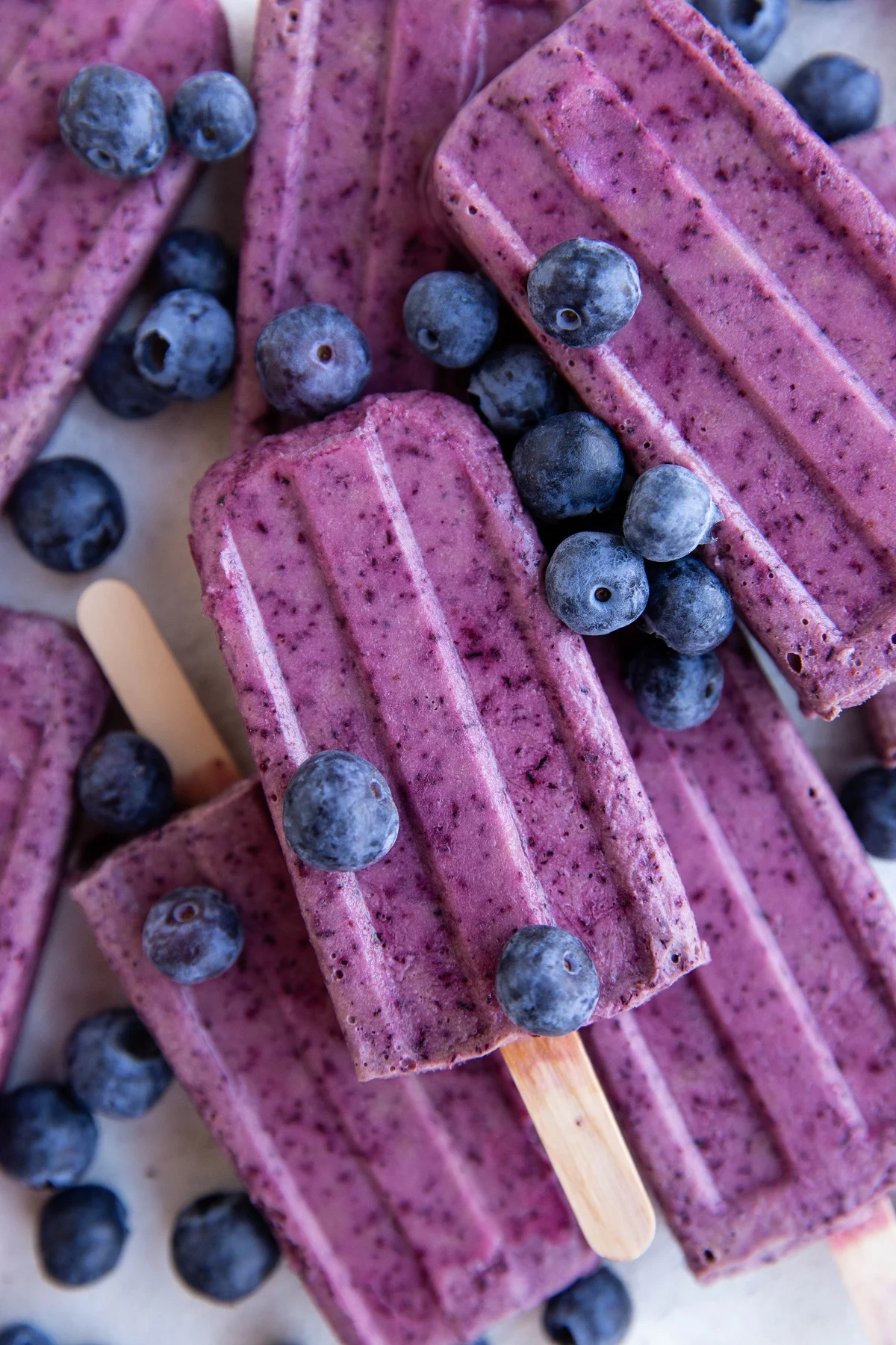 Stack of blueberry coconut milk popsicles with fresh blueberries all around.