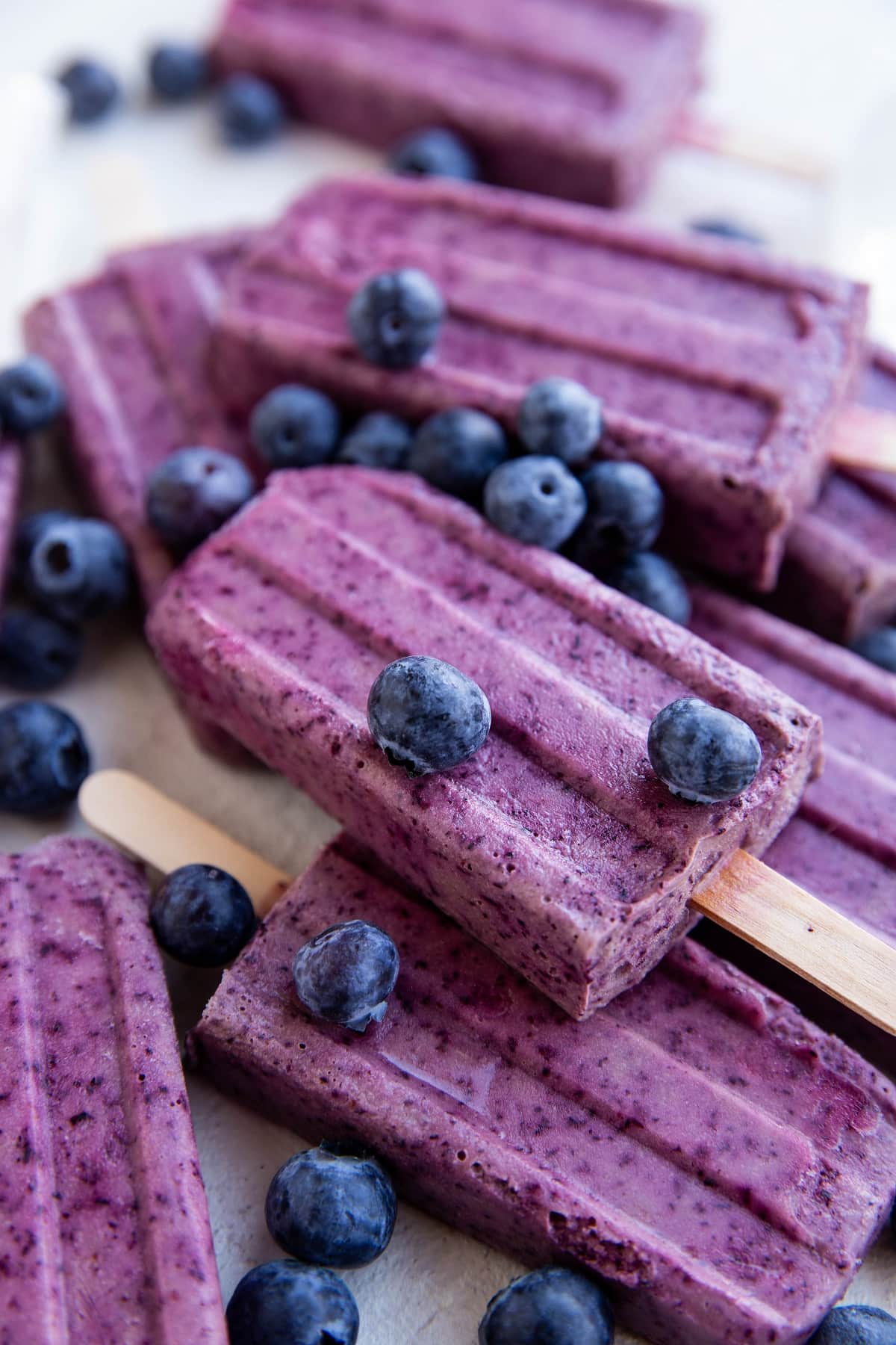 Pile of blueberry coconut milk popsicles with fresh blueberries all around.