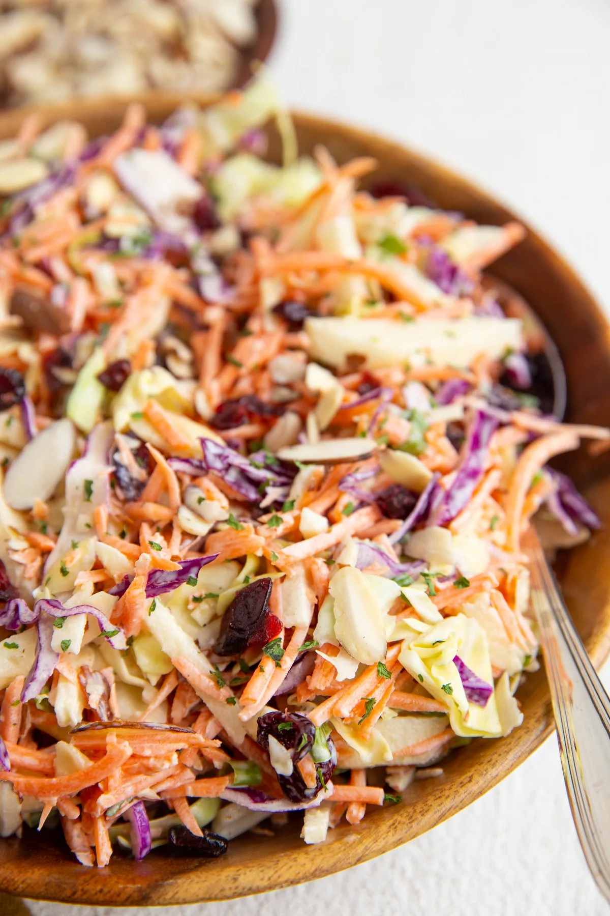 Big wooden bowl full of carrot slaw with a spoon to the side, ready to serve.
