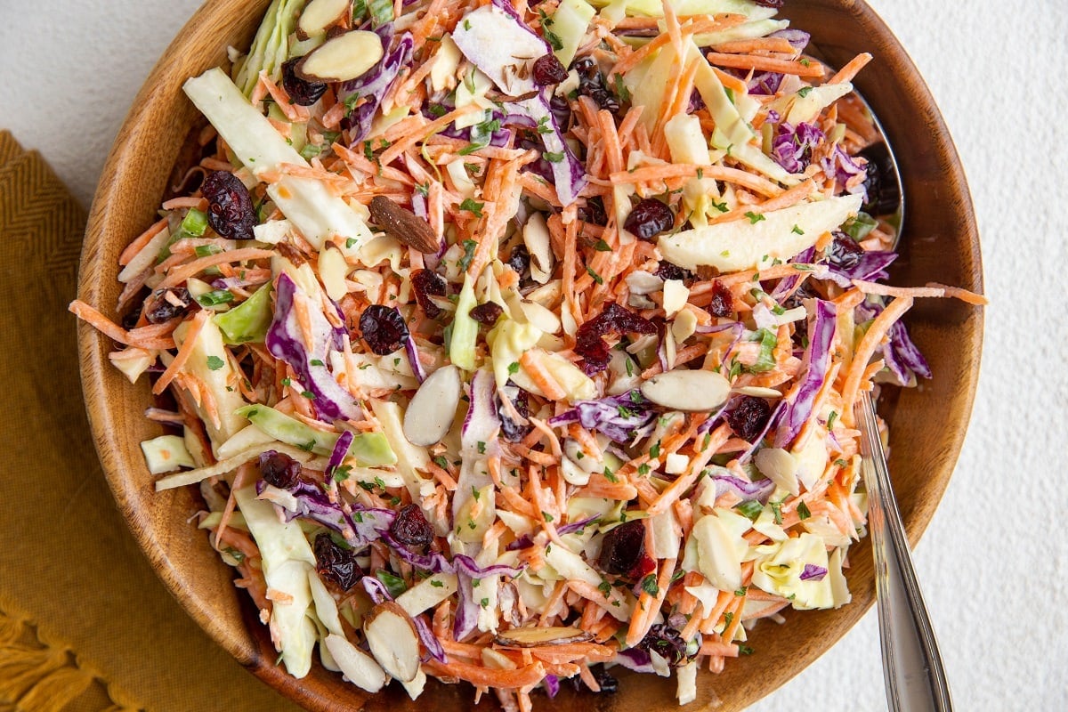 Wooden bowl of carrot apple slaw with cabbage, dried cranberries and green onion.