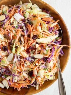 Big wooden bowl with carrot coleslaw inside and a spoon, ready to serve.