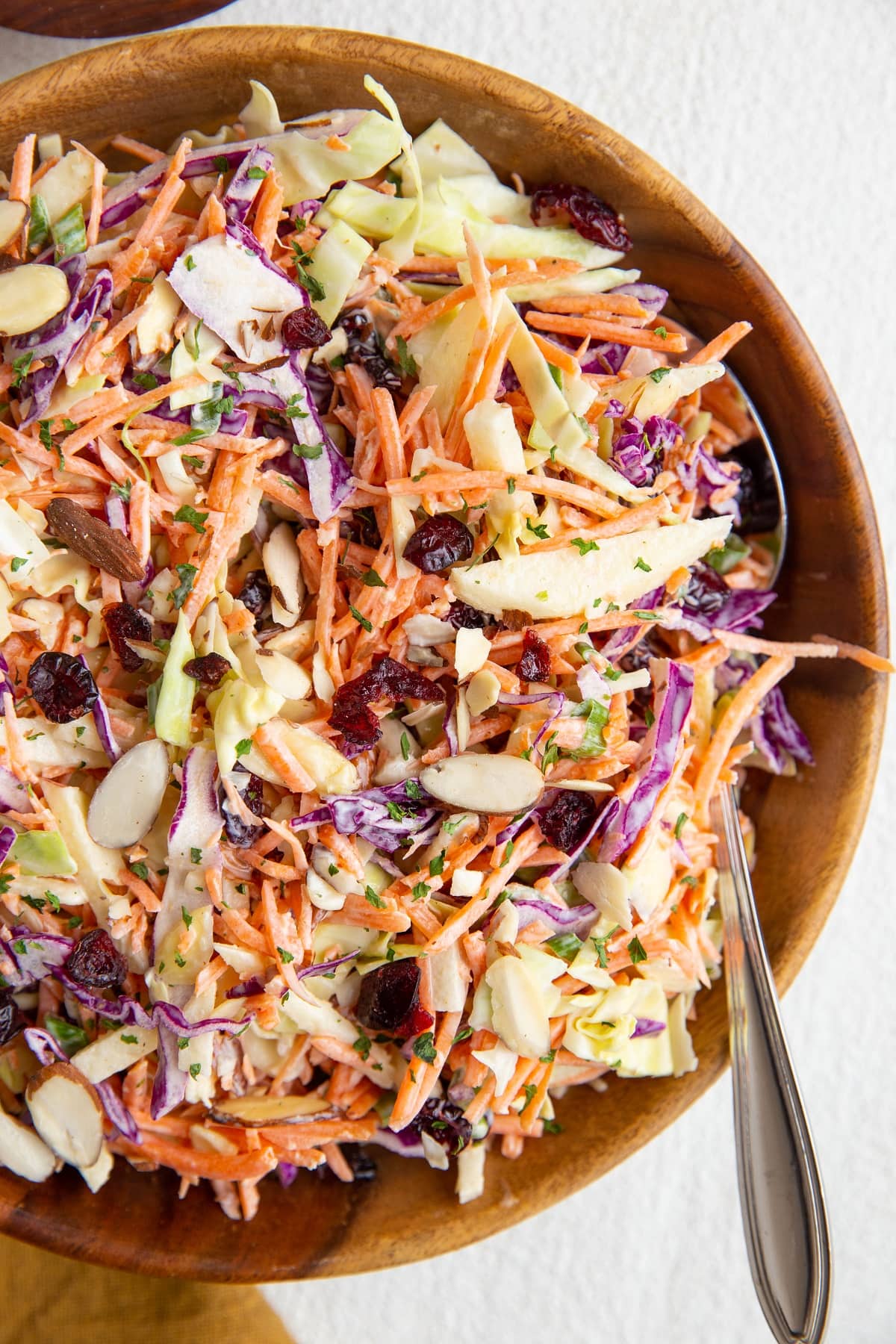 Big wooden bowl with carrot coleslaw inside and a spoon, ready to serve.