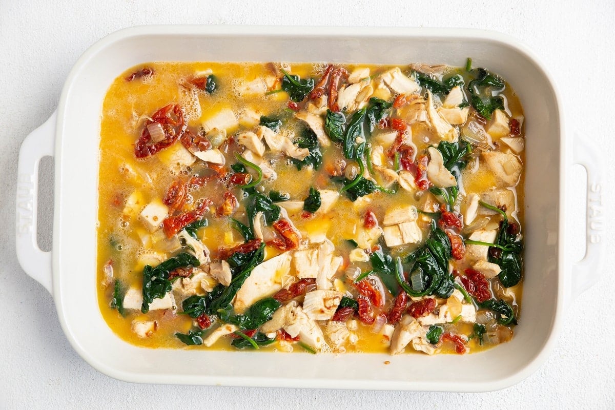 Casserole dish with chicken, vegetables and raw eggs for egg bake.