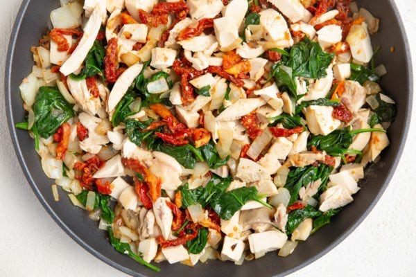 Skillet with onion, spinach, sun-dried tomatoes, chicken and garlic.