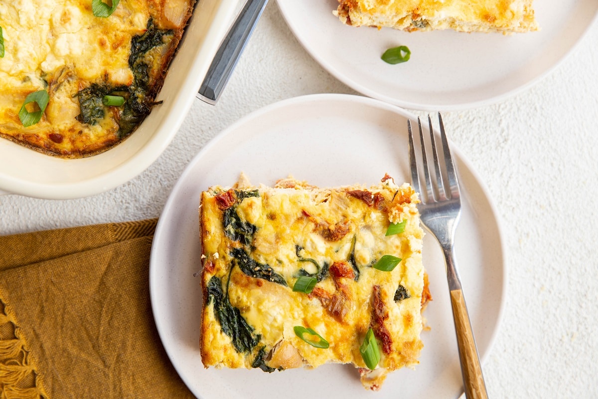 Slices of breakfast casserole on white plates with forks, ready to eat.