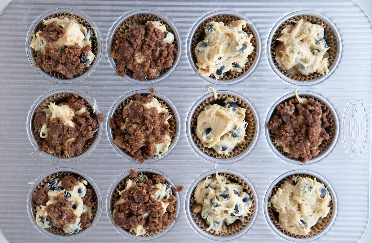 Muffin batter sprinkled with streusel topping in a muffin tin.