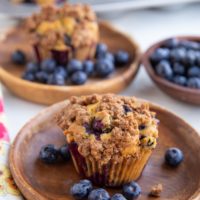 Two blueberry muffins on wooden plates, ready to eat.