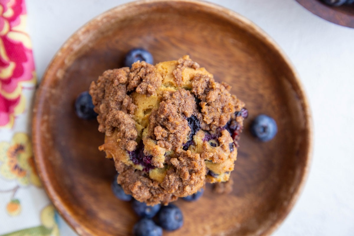 One blueberry muffin on a wooden plate with fresh blueberries to the side.