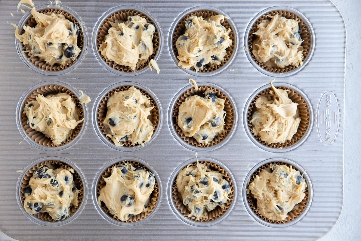 Blueberry muffin batter inside of muffin cups of a muffin tray, ready to bake.