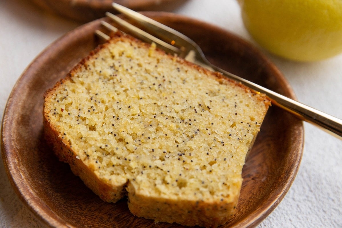 Wood plate with a slice of moist lemon poppy bread on it with a gold fork.