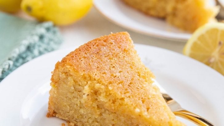 Two slices of lemon cake on two plates with fresh lemons all around.