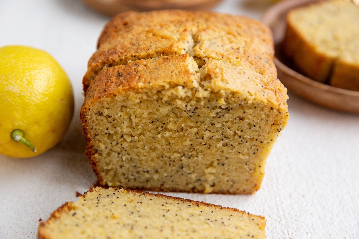 Lemon loaf cut into slices with a plate in the background with a slice on it.