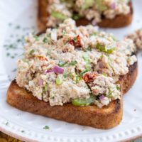 Two slices of toasted bread on a plate with tuna salad on top.