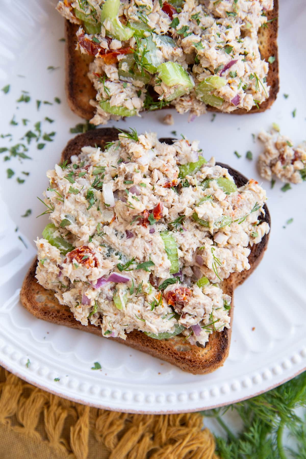 Two slices of toasted bread on a white plate with tuna salad on top.