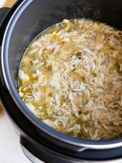 Instant Pot full of shredded chicken in green sauce for tacos or burritos.