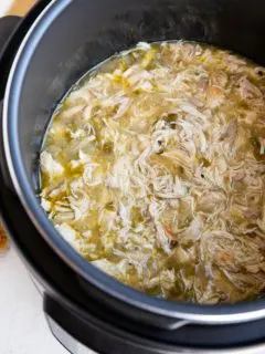 Instant Pot full of shredded chicken in green sauce for tacos or burritos.
