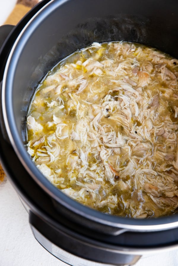 Instant Pot full of shredded chicken in green sauce for tacos or burritos.