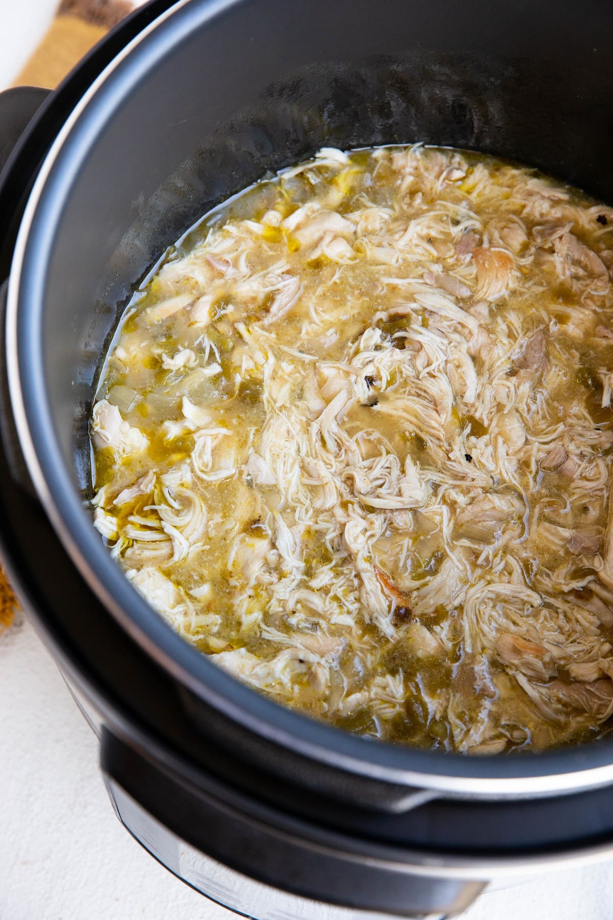 Instant Pot full of shredded chicken in green sauce for tacos or burritos.