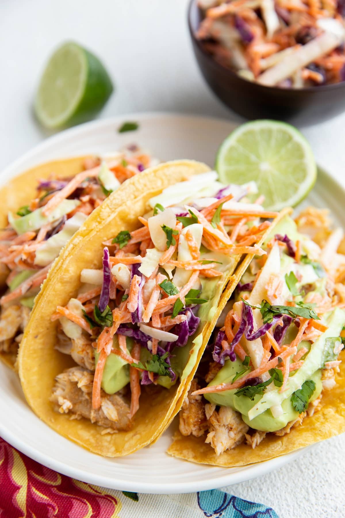 Three fish tacos on a plate with slaw in the background.