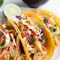 Three fish tacos on a plate with slaw and avocado sauce.