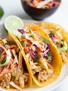 Three fish tacos on a plate with slaw and avocado sauce.