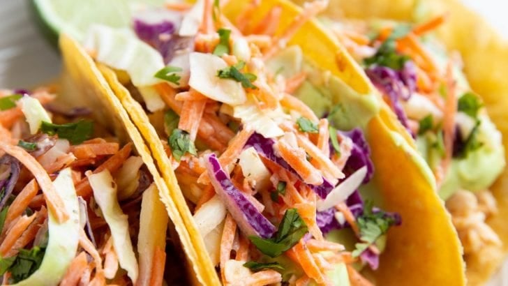Three fish tacos on a plate with slaw and avocado sauce.